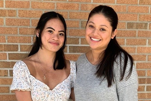 two young women stand in front of a brick wall